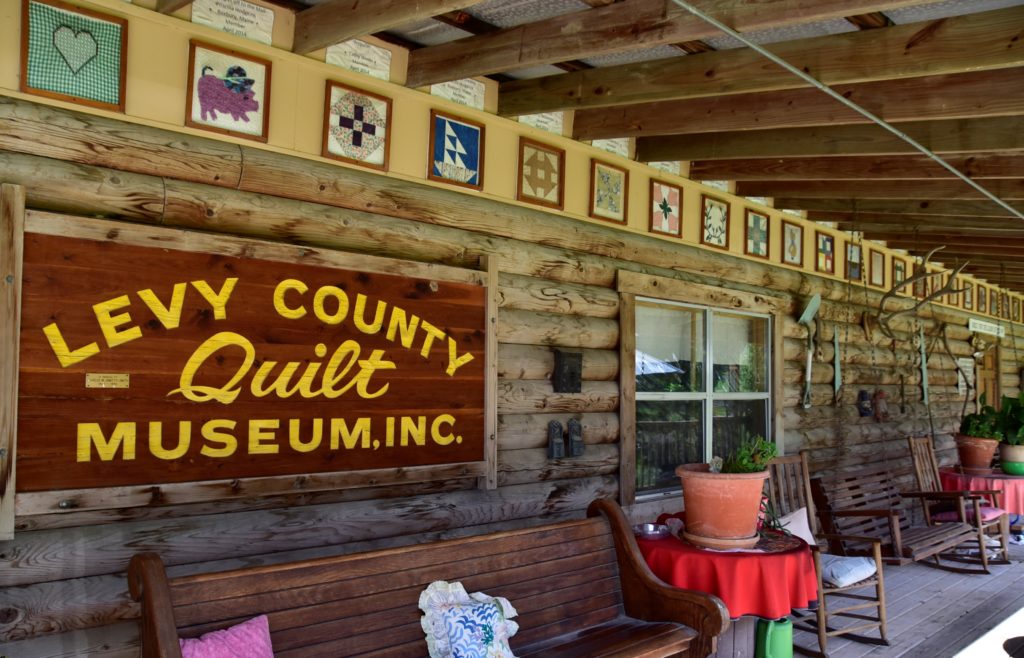 Log cabin porch with old benches and framed quilt pieces across the top border