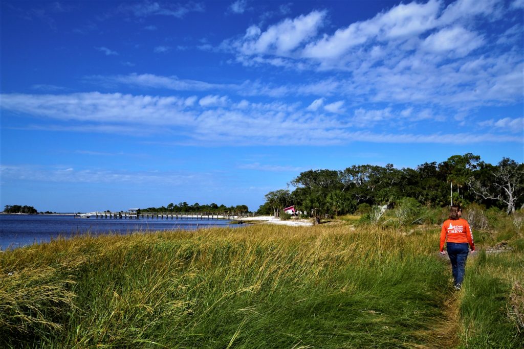 Woman walking a path in the grass along the Gulf toward a pier