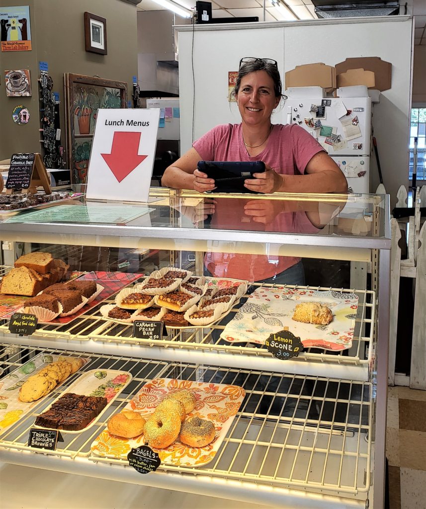 glass case filled with dessert choices, woman owner leaning on top of the case