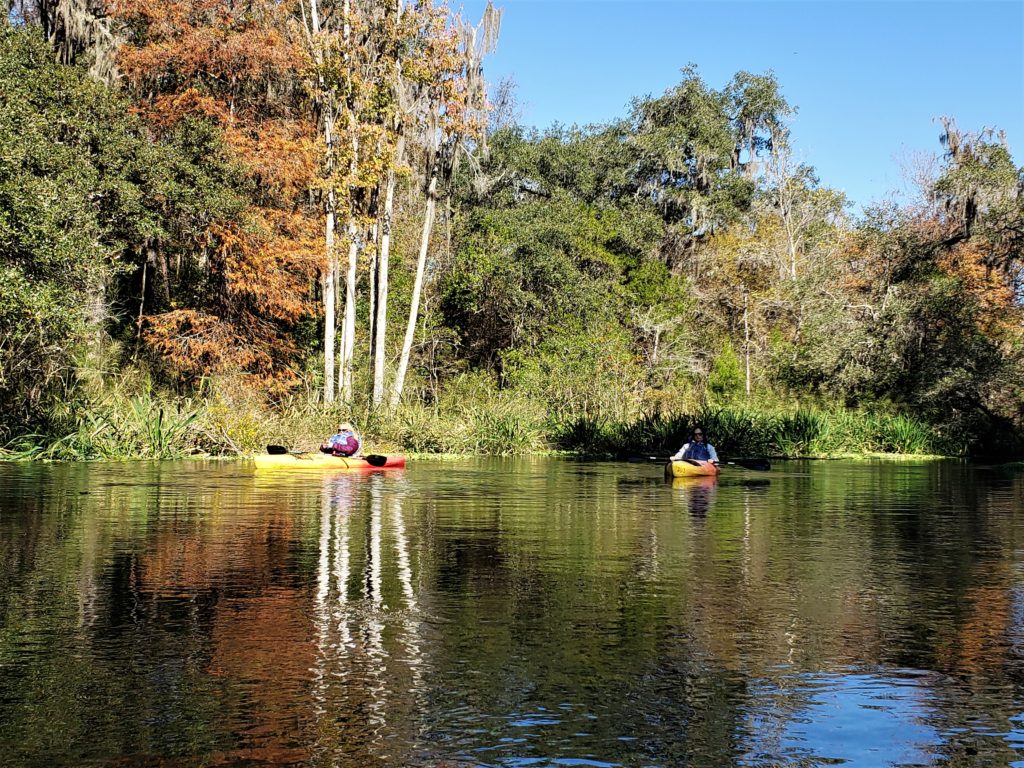 two kayakers coming down river, blue sky and reflecting on water