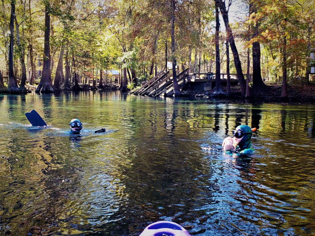 two divers surfacing in the spring in front of a kayak