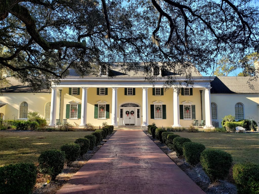 The museum building - a large yellow house, green shutters two-story with columns and front porch two stories tall 