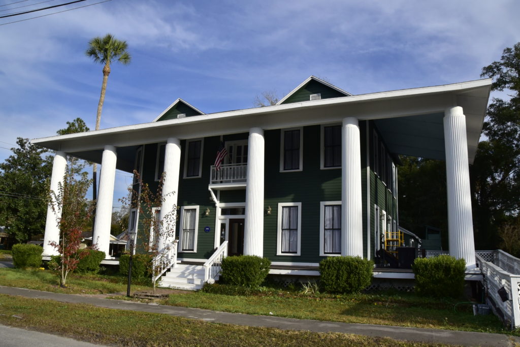 Large green greek revival house with two story tall columns
