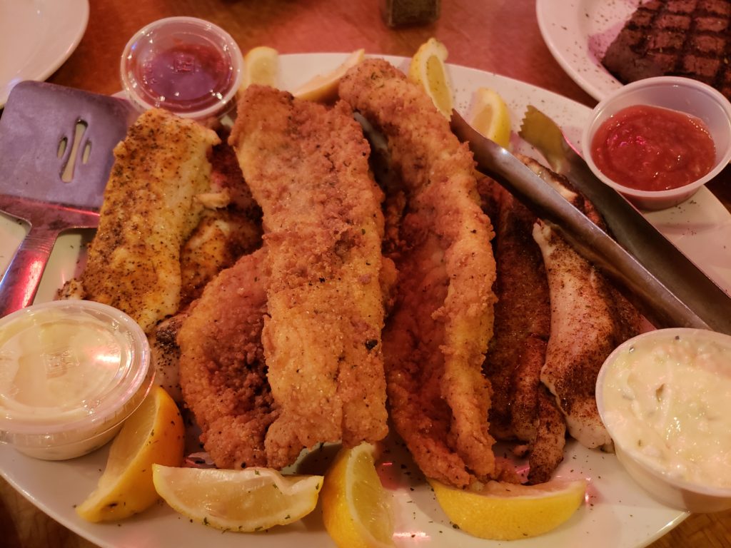 a piled-up platter of Fried, blackened, and grilled Sea Trout from a day's fishing with condiments and lemon segments