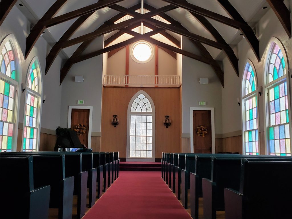 A view of the interior of a chapel with stained glass windows and dark wooden pews