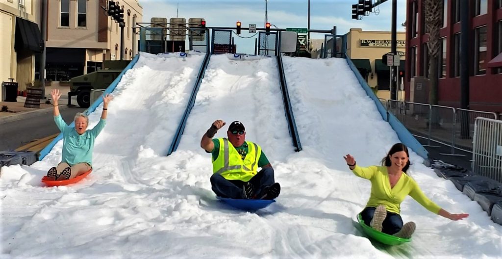 3 people sliding down man-made hill of snow
