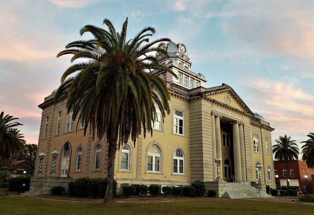 Courthouse with palm trees on lawn, pink sunset sky behind
