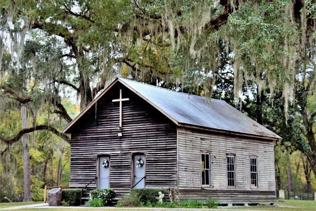 old unpainted natural weatherd wood church among oak trees and moss